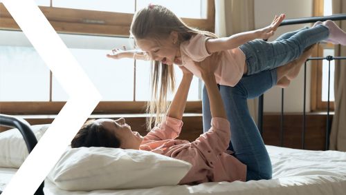 Woman holding her daughter in the air with her feet and arms while laying on the bed (like Superman)