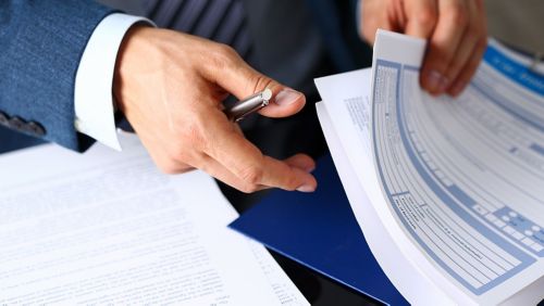 A man's hands looking through business forms while holding a pen.