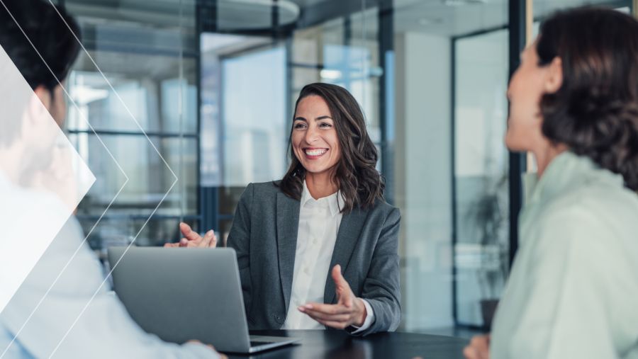 A businesswoman laughing with coworkers at a table while on a laptop