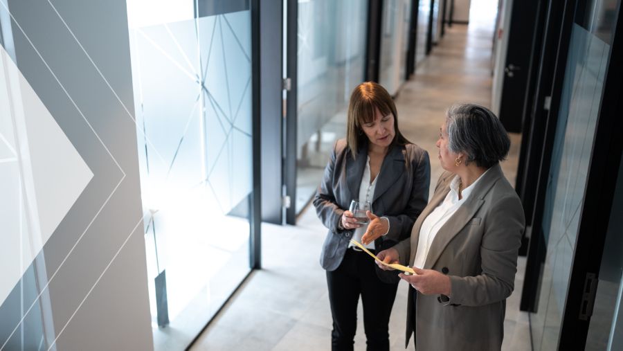 Two coworkers discuss out of a conference room in an office