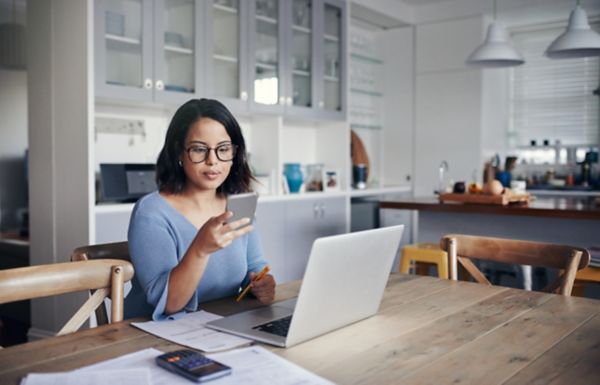 A woman researching EBPP solutions on her cell phone with a laption in front of her. 