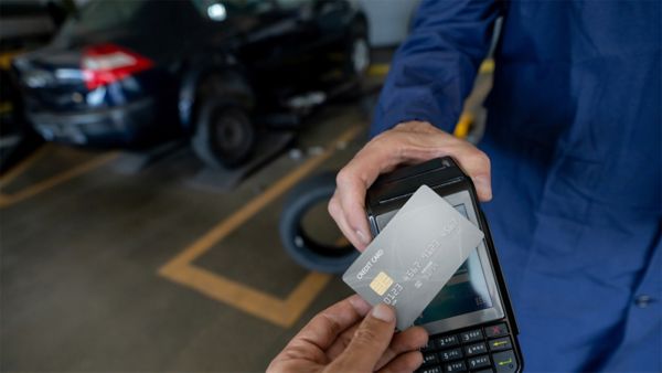 A hand holding a credit card and using tap-to-pay on a credit card terminal. 