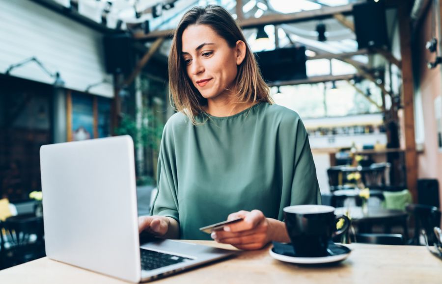 A woman sits at a laptop holding a credit card, ready to make an online payment