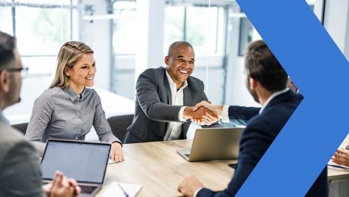 business associates shake hands while seated at a table 