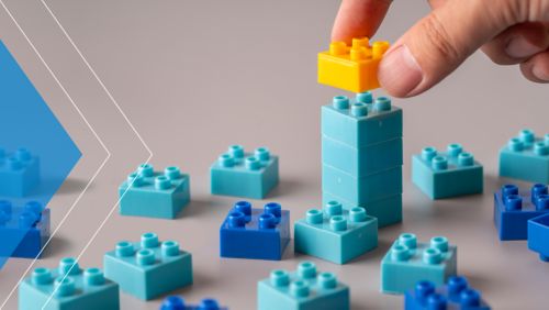 Hand placing a yellow plastic building brick on top of a tower of blue bricks.