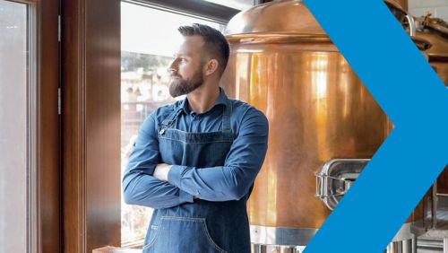Man looks out window standing in front of distilling tanks