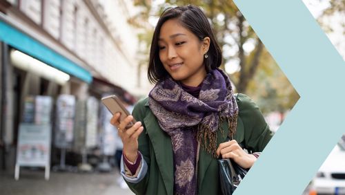 Low angle portrait of young businesswoman managing a digital payment on her mobile phone against corporate skyscraper background.