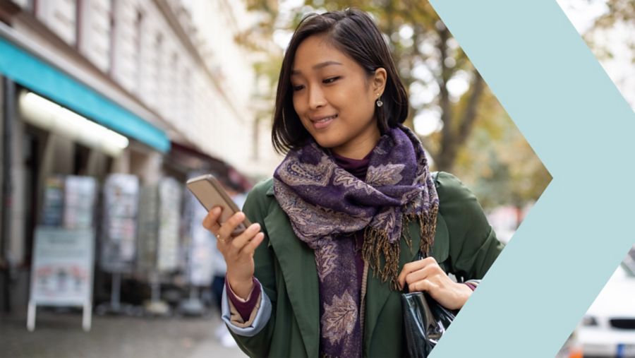 Low angle portrait of young businesswoman managing a digital payment on her mobile phone against corporate skyscraper background.