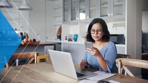 Woman on her phone at her laptop in the kitchen.