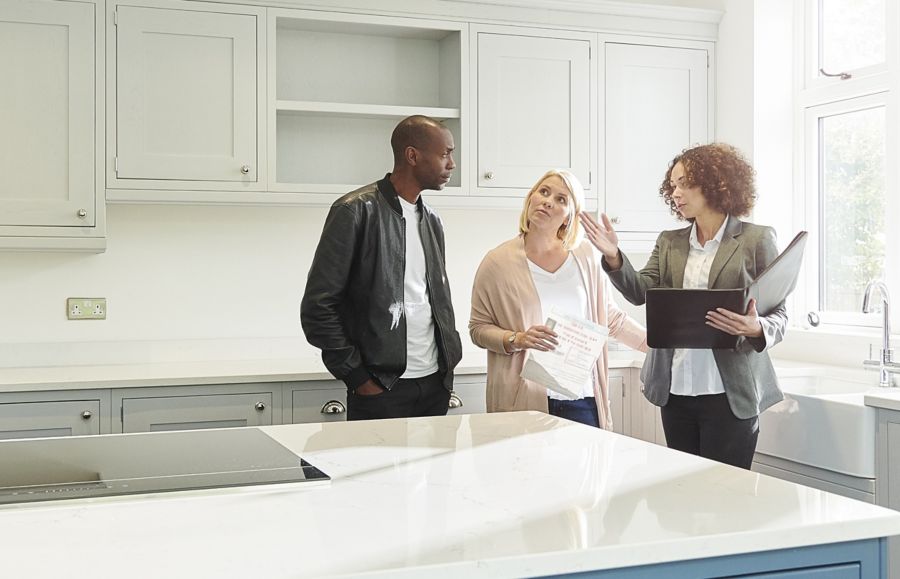 A real estate agent discusses a property with two prospective buyers in an empty kitchen