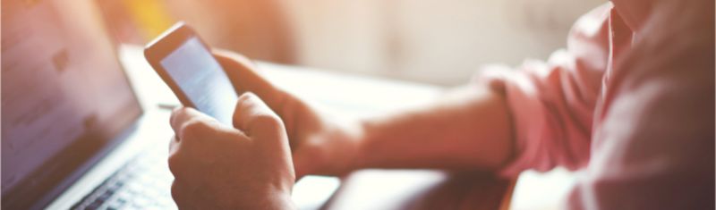 A person using a mobile phone while also on a laptop