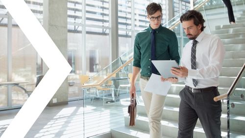 Two men walking down office stairs while reviewing information on tablet