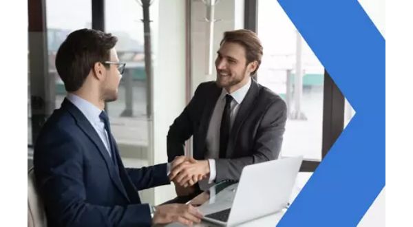 Two business colleagues shake hands while sitting on either side of a laptop