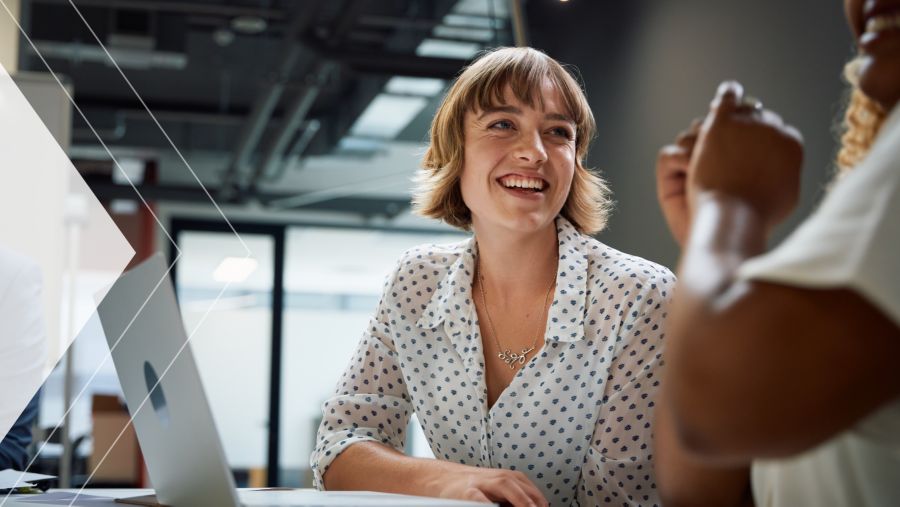 A woman working on a laptop and having a conversation with a coworker