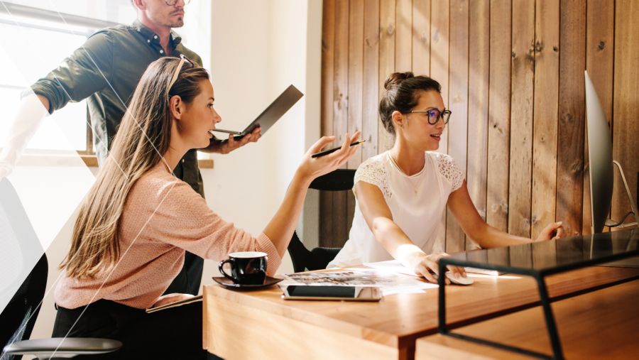 A woman working on a desktop computer with two of her coworkers