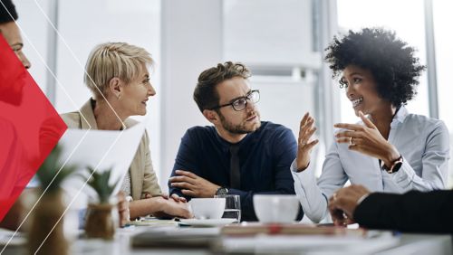A businessman sitting in a conference room with other colleagues talking while using his hands.