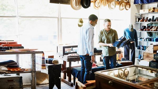 A male shop owner showing a male customer a pair of blue jeans. 