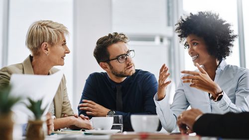 A businessman sitting in a conference room with other colleagues talking while using his hands.